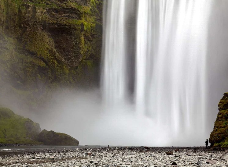 Islândia, pessoa junto à queda de água da cascata Skógafoss