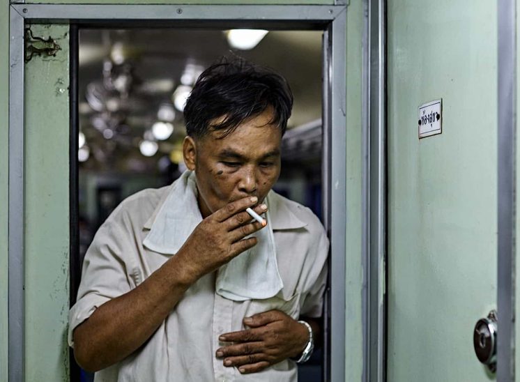 Tailândia, homem a fumar entre as carruagens de um comboio