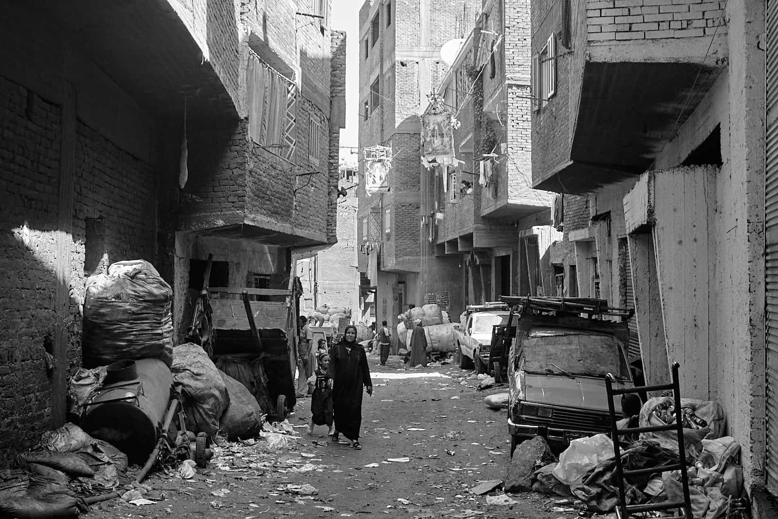 Mokattam Zabbaleen, mulher e filha a percorrer uma uma rua cheia de lixo