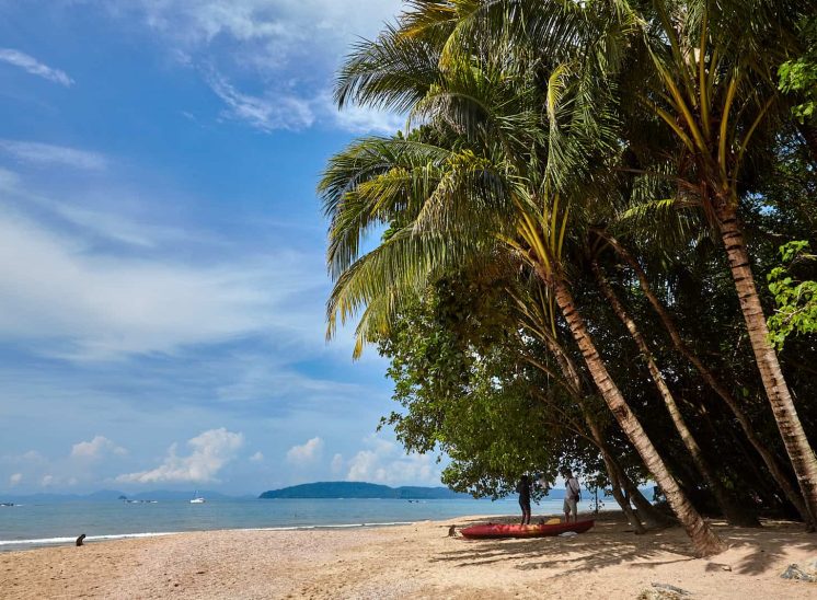 Tailândia, pessoas a conversar sob palmeiras na praia Ao Nang