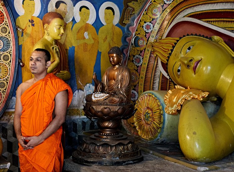 Sri Lanka, monge a orar junto à estátua de Buda dentro de um templo
